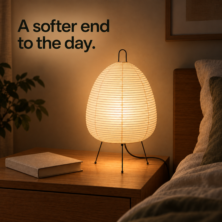 Paper table lamp casting warm light beside linen bedding